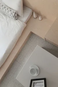 A minimalist bedroom with white bedding and wooden furniture.