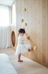 A toddler climbing on a wooden wall with yellow climbing holds in a modern children's playroom.