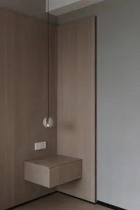 A minimalist floating shelf with a spherical light fixture hanging above it, set against a wooden wall and a grey wall.