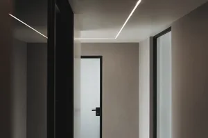 A modern corridor featuring concrete walls and floor with linear LED lighting fixtures.