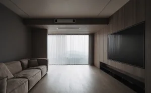 Modern minimalist living room featuring wooden walls and furniture, large television, and floor-to-ceiling windows with verti