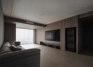 A modern minimalist living room with a wooden floor, a large television mounted on a wooden wall, and a cozy sofa.