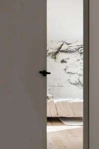 A minimalist bedroom featuring a concrete wall with a large, detailed wall mural of a classical statue's head, a bed with a t