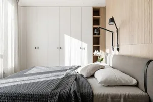Modern minimalist bedroom featuring a grey upholstered bed against a wall of light wood panels and a large white wardrobe.
