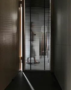 A modern doorway with metal blinds partially open, showing a wooden floor and a person standing behind the blinds.