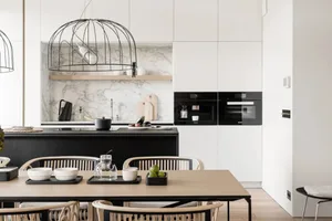 A modern, minimalist kitchen with wooden dining table, marble backsplash, and metal pendant lights.