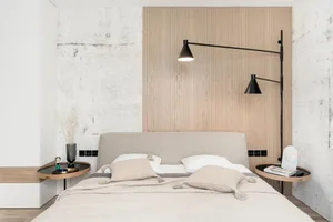 A modern minimalist bedroom with a light-colored bed, wooden headboard, and industrial-style wall lamps.