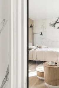 A modern minimalist bedroom featuring marble and wood materials, with a large bed and floating nightstands.
