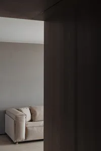 Modern living room featuring a beige couch with pillows, situated in a minimalist space with light-colored walls and floor.