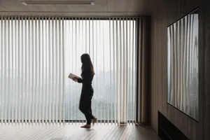 A person walking between vertical blinds with a wooden panel wall