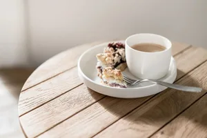 A white cup and plate with food and a fork on a wooden table