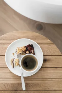 A piece of blueberry coffee cake on a plate with a cup of coffee on a wooden table.