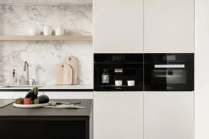 A modern minimalist kitchen with white matte cabinets, a black countertop, and a marble backsplash.