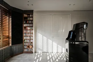 A modern living room featuring a bookshelf filled with books and a large black gaming cabinet, with light streaming through t