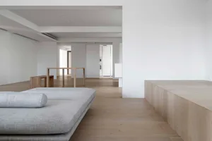 A modern minimalist living room with light wooden floors, a grey sofa, and a low wooden bench, featuring clean lines and a mo