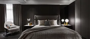 A modern residential bedroom featuring textured fabric upholstery on the bed and armchair.