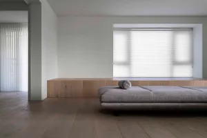 Modern minimalist living room with wooden flooring, fabric furniture, and large window with blinds.
