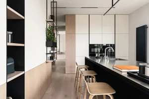 Modern minimalist kitchen featuring metal countertops, wooden stools, and glass cabinetry.