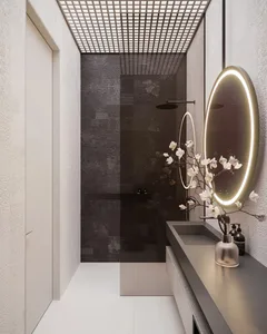 Modern bathroom with dark tiled walls, a sleek sink counter, and a round mirror with illuminated edges.