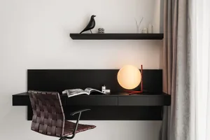 A modern black wood home office setup with a leather chair, minimalist desk, and green plant.