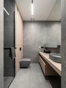 Modern, minimalist bathroom with concrete walls and floor, featuring a floating wooden vanity with a round sink and a closed-