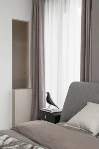 A modern grey bedroom featuring a grey upholstered bed with a bird sculpture on a bedside table.
