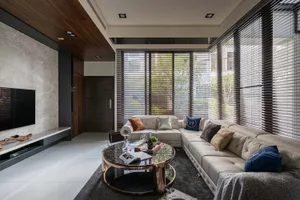 A modern living room featuring a large leather sofa, a glass coffee table, and a flat-screen TV on a marble wall.