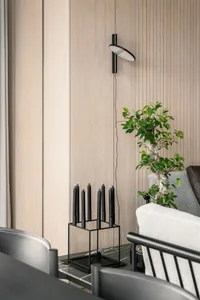 A modern living room featuring a wood-paneled wall, a contemporary floor lamp, a green bonsai tree, and minimalist furniture.
