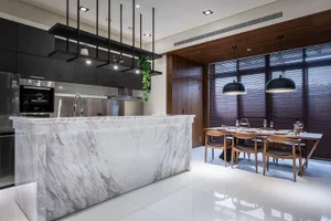 A modern residential living space featuring marble countertops, wooden dining chairs, and stainless steel appliances.