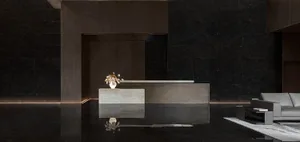 A modern lobby with a concrete reception desk, white vase with flowers, and a grey sofa on a white rug.