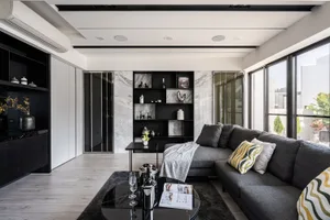 A modern minimalist living room featuring a grey sofa, marble accent wall, and sleek black accents.