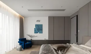 A modern minimalist bedroom featuring a blue armchair, a bed with a fur blanket, and a gray wardrobe.