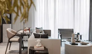 A minimalist living room featuring a cream-colored sofa, a round coffee table, and a white desk with a black and white table 