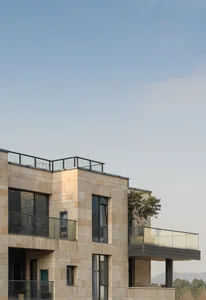 Modern, minimalist residential building with stone exterior, glass windows, and rooftop balcony.