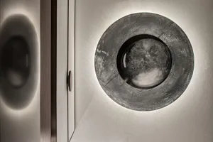 A modern interior design featuring a round, textured concrete lighting fixture mounted on a white wall.