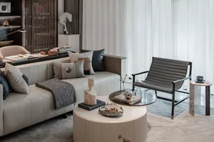 A modern living room with neutral-toned furniture, including a white sofa with patterned pillows, a glass coffee table, and a