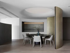 A modern dining room with a round table, white chairs, and a metal partition, featuring a minimalist design and lighting.