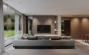 A modern living room featuring a concrete and stone wall with a large sofa and large windows looking out to greenery.