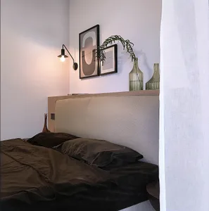 A cozy, minimalistic bedroom featuring dark textiles, a structured headboard, and a wall-mounted light fixture.