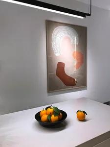 A modern minimalist kitchen with abstract art, oranges, and white countertops.