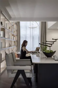 A modern, minimalist residential workspace with a sleek table, gray chairs, natural light, and an open layout.