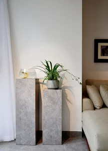 A modern living room with concrete pedestals, houseplants, and a neutral couch.