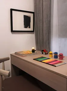 Modern home office featuring a wooden desk with colorful pencils and toys, a framed abstract artwork, and gray curtains.