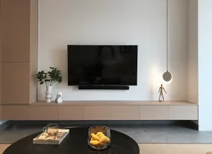 A modern living room with wooden furniture, a round black coffee table, and a flat-screen TV mounted on the wall.