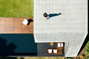 A modern, minimalist exterior features concrete tiles and wooden elements. A person walks on the rooftop patio.