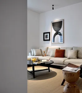 A minimalist living room featuring a white couch, a round black coffee table with a glass vase of lemons and two books, and a