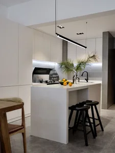 A modern minimalist residential kitchen featuring white cabinets, a white countertop, and a white island with black stools an