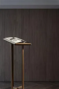 A modern, wooden bookstand holding an open book against a dark, wood-paneled wall.