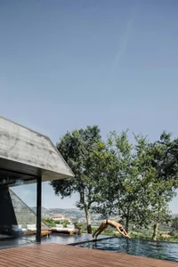 A modern house with a concrete exterior and infinity pool surrounded by greenery.