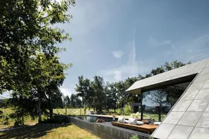 Modern minimalist outdoor living space with a concrete patio and pool, surrounded by greenery and trees, and featuring a slee